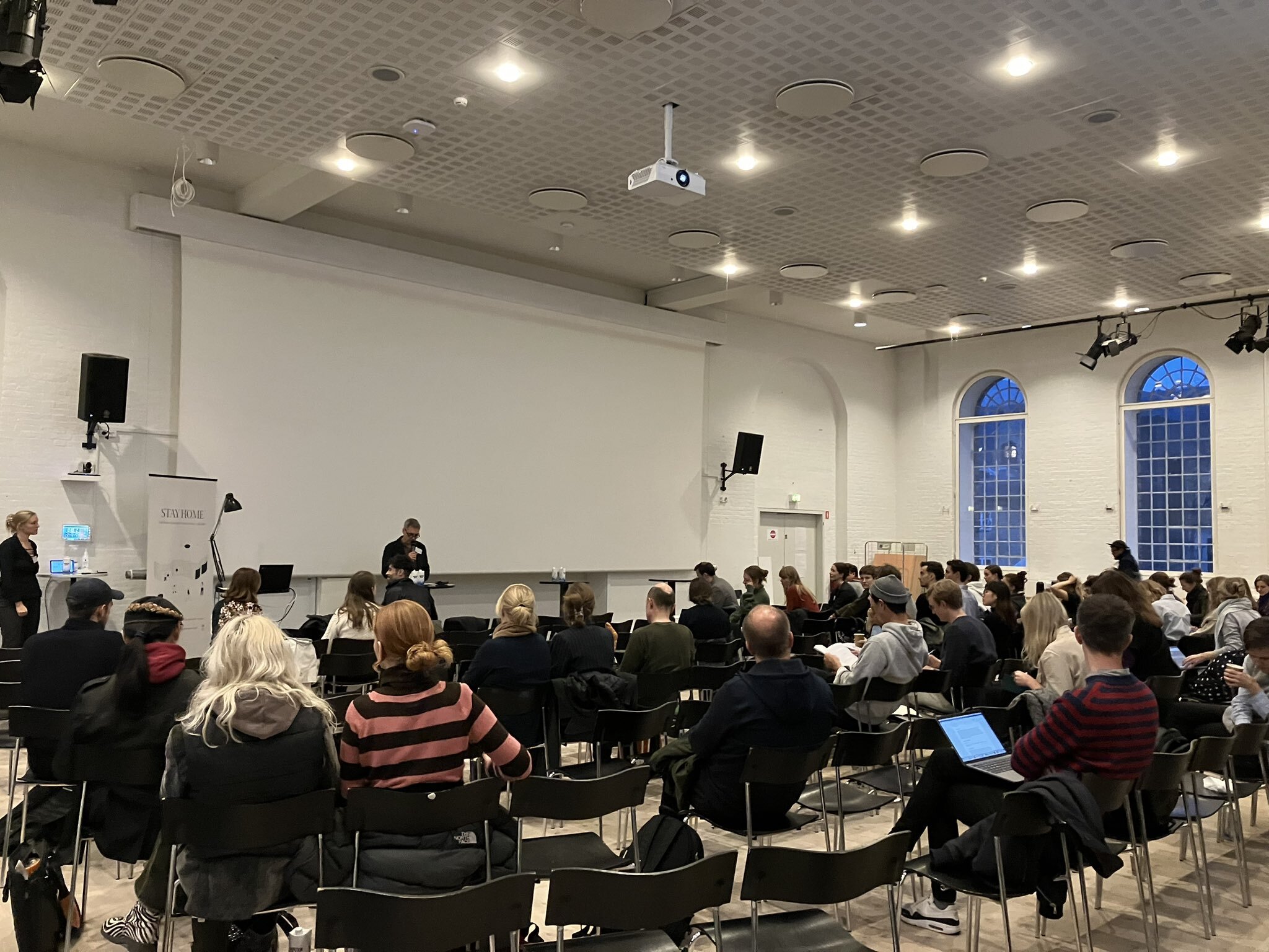 A picture of the audience from behind looking at Co-PI at STAY HOME Peter Thule Kristensen presenting a keynote speaker